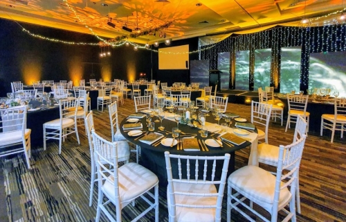 Star ceiling canopy of greenery branches, black wrought iron pendant lights and fairy lights Tiffany chairs, black table cloths, Fairy light curtain backdrop to stage, Pacific Bay Resort Reef Room