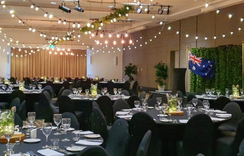 Jetty Harbour Marina Rooms - Marquee ceiling canopy, greenery & Festoon lights, Edison chandeliers, Black chair covers, Table decoration glass vase  battery fairy lights, eucalyptus, babies breath on a timber log- Pacific Bay Resort