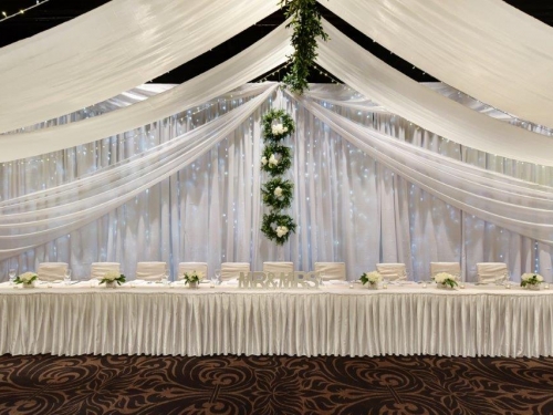 Bridal table fairy light backdrop greenery wreaths + ceiling canopy marquee style with greenery spine