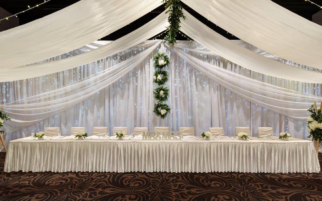Bridal table fairy light backdrop greenery wreaths + ceiling canopy marquee style with greenery spine
